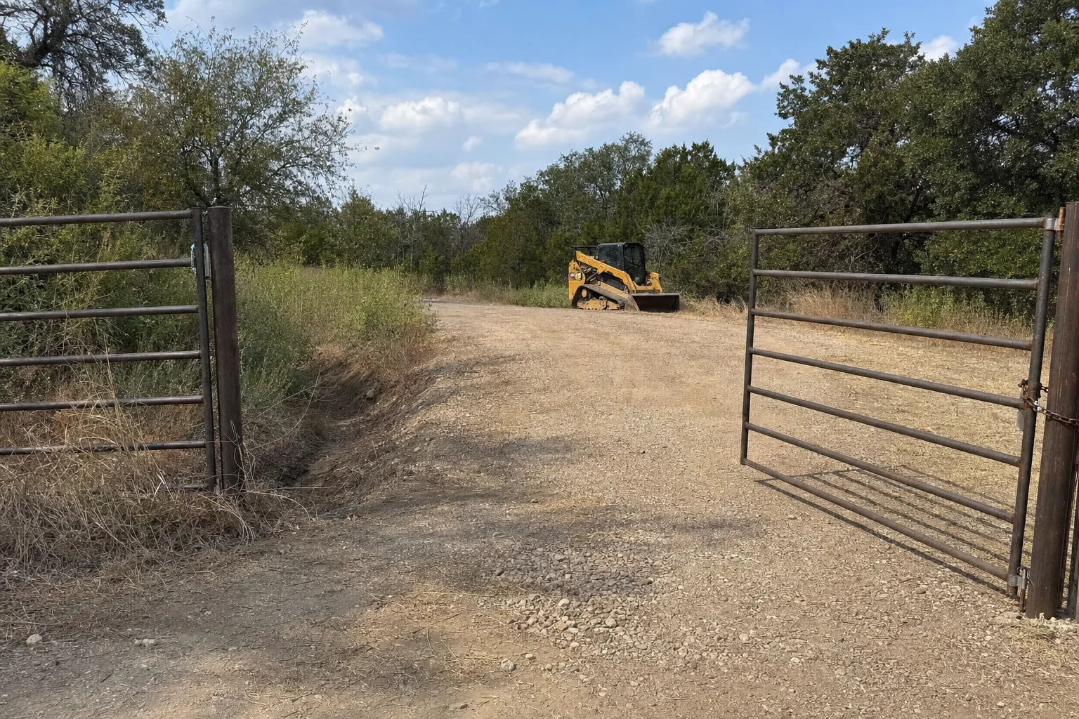 An open pipe gate shows the gravel entrance and parked track loader.