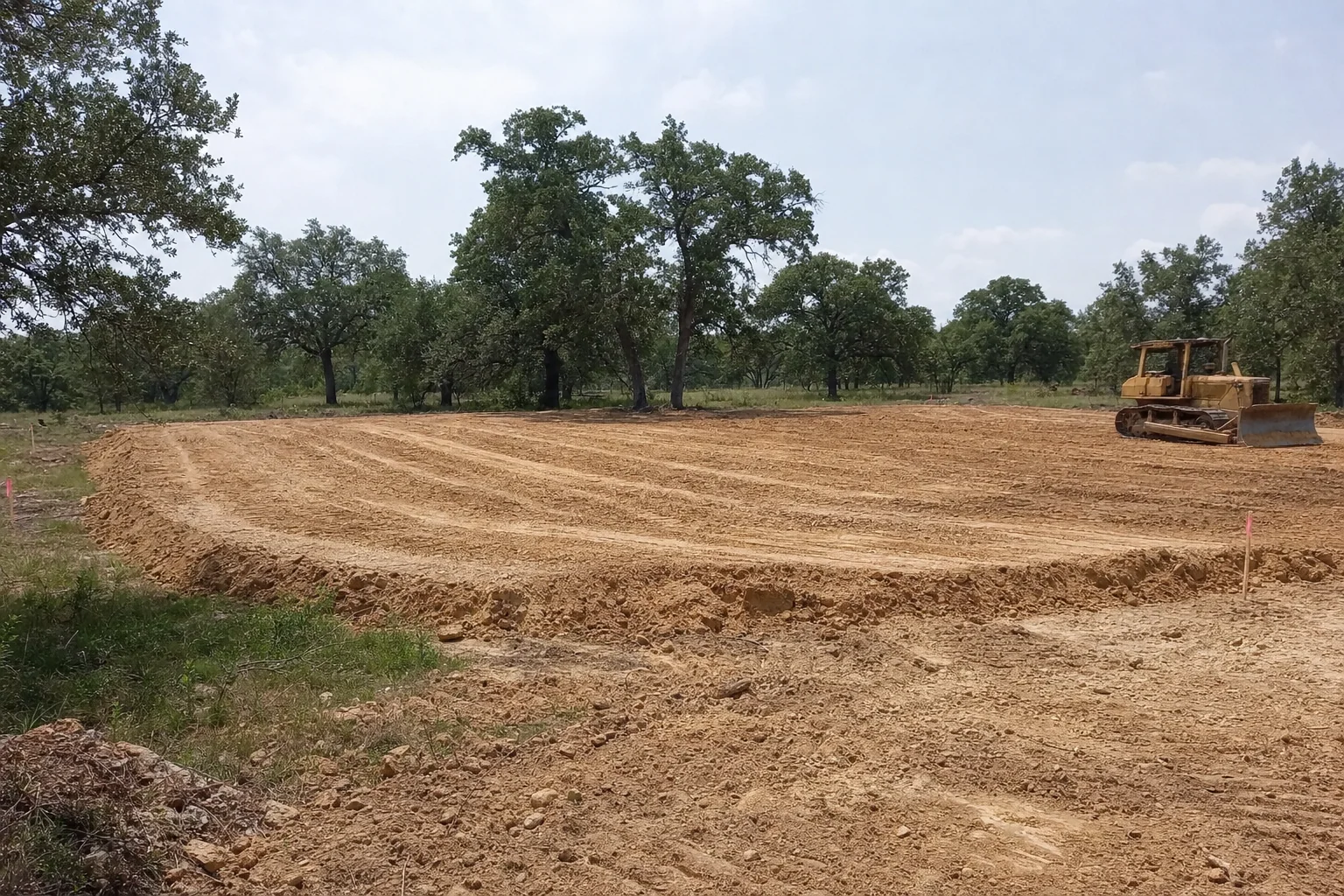 A dozer sits beside the rough pad with fill tracks across the top.