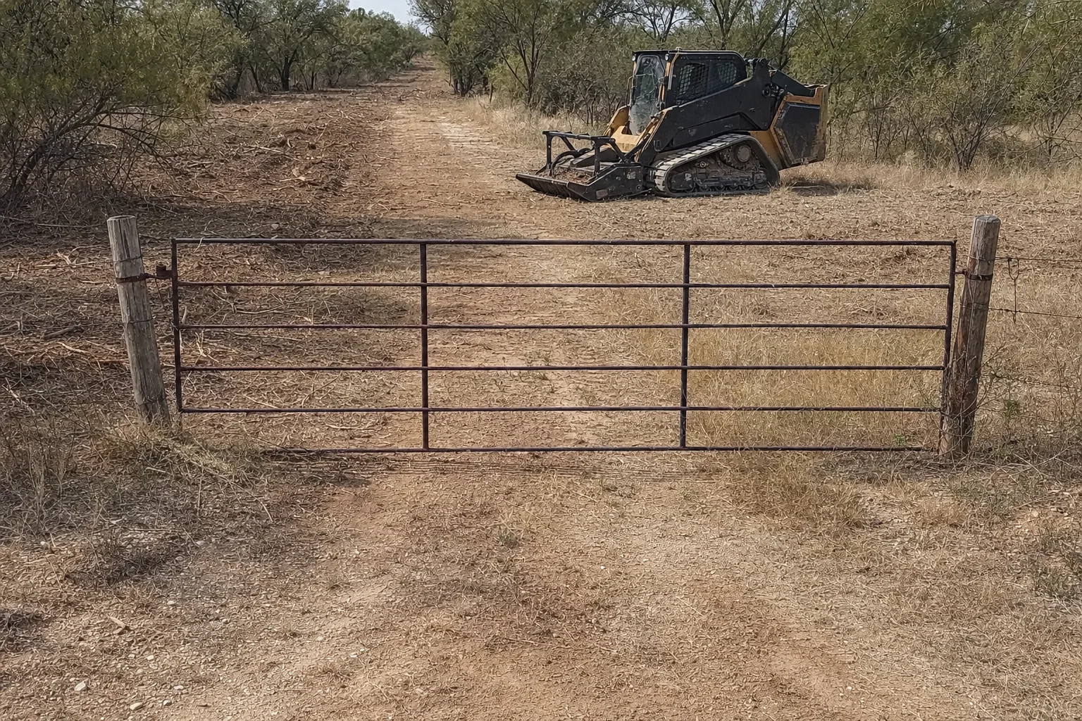 Beyond the pipe gate, a cleared lane runs through dry mesquite cover.