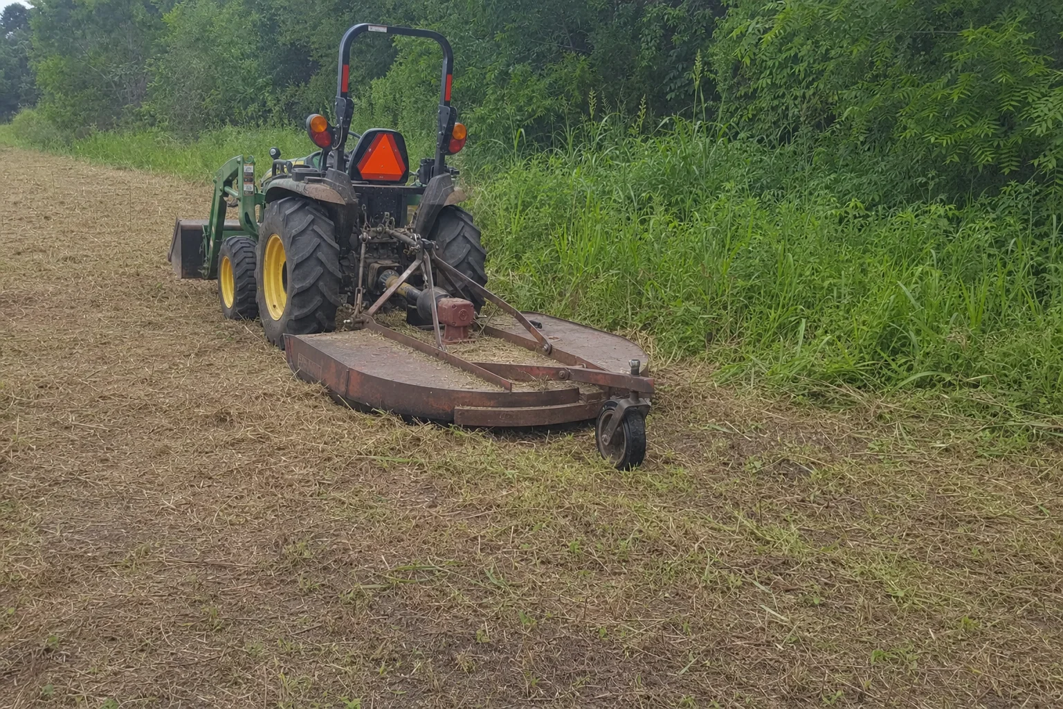 The rear cutter rests beside tall grass and coarse mowing clippings.
