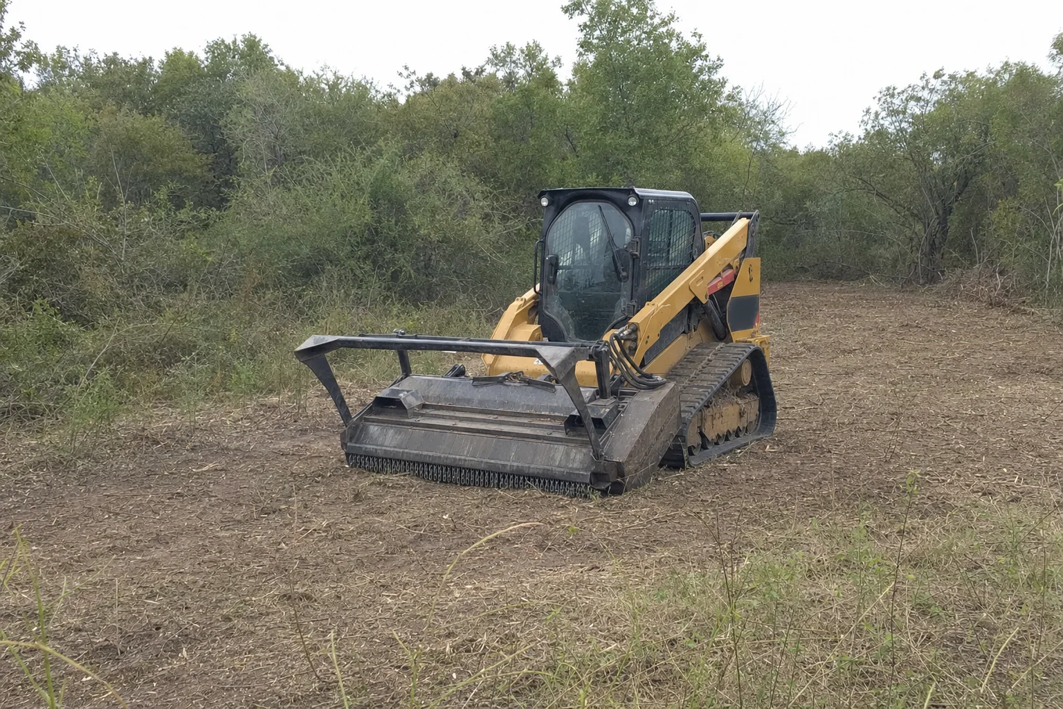 Rough grass edges the cleared strip beside the lowered brush head.
