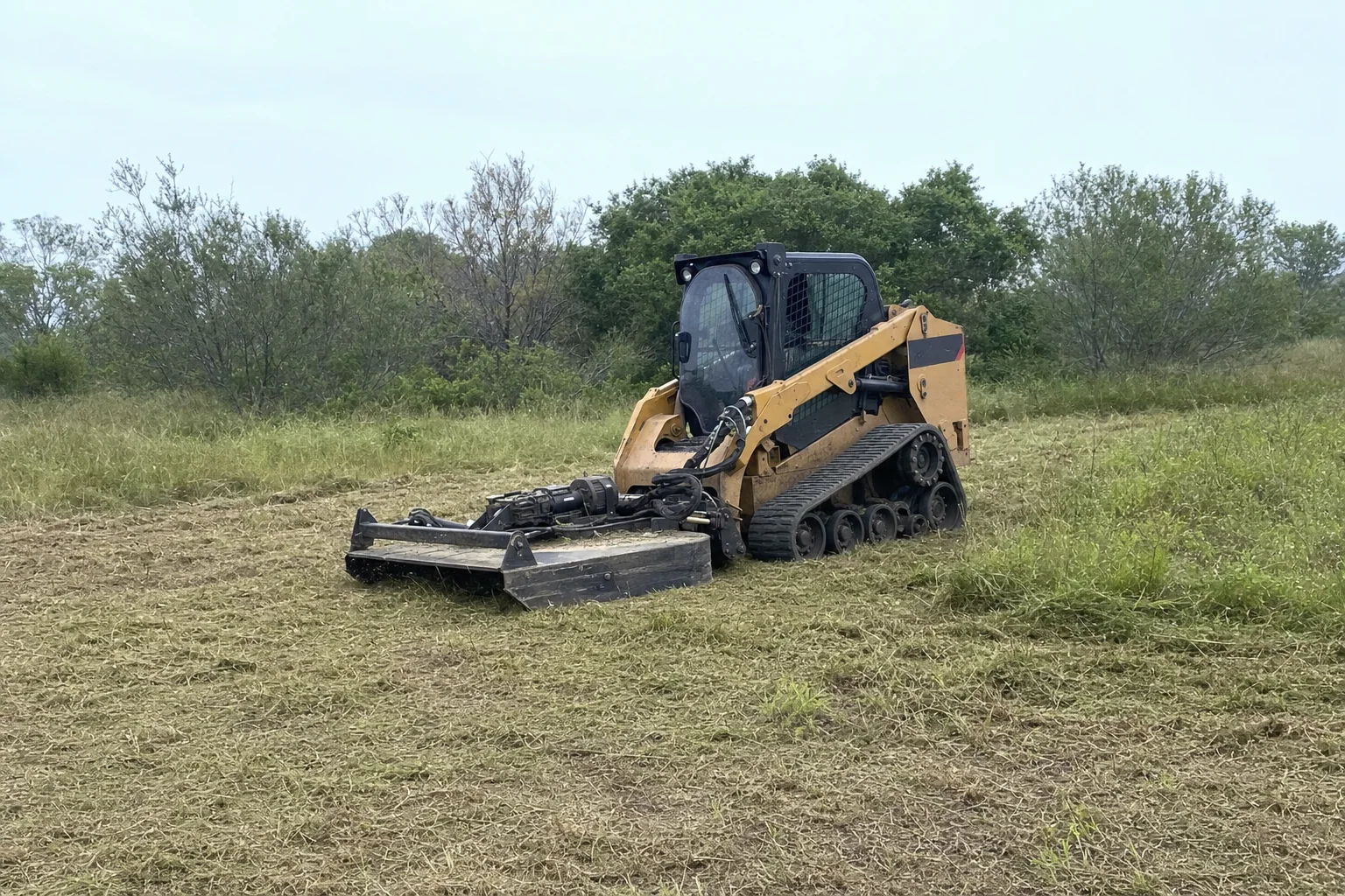 Coarse clippings surround the rotary cutter beside taller grass and low brush.