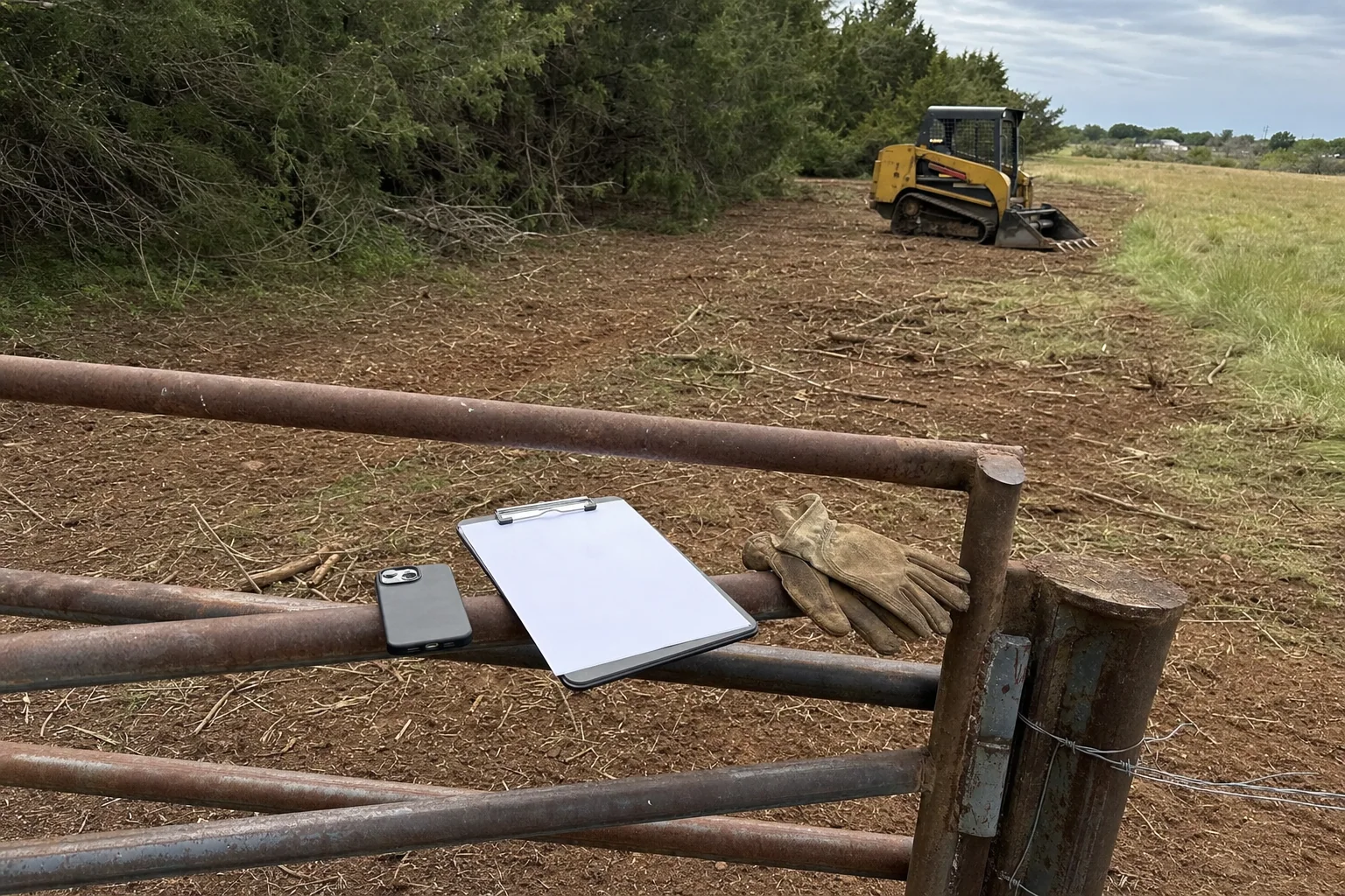 A blank clipboard and gloves rest on the gate above cleared brush.