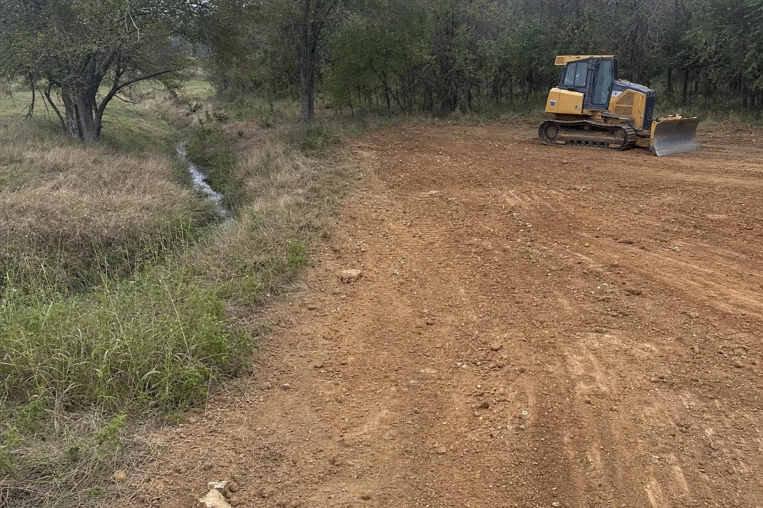 Rough grade ends beside a grassy channel holding a little water.