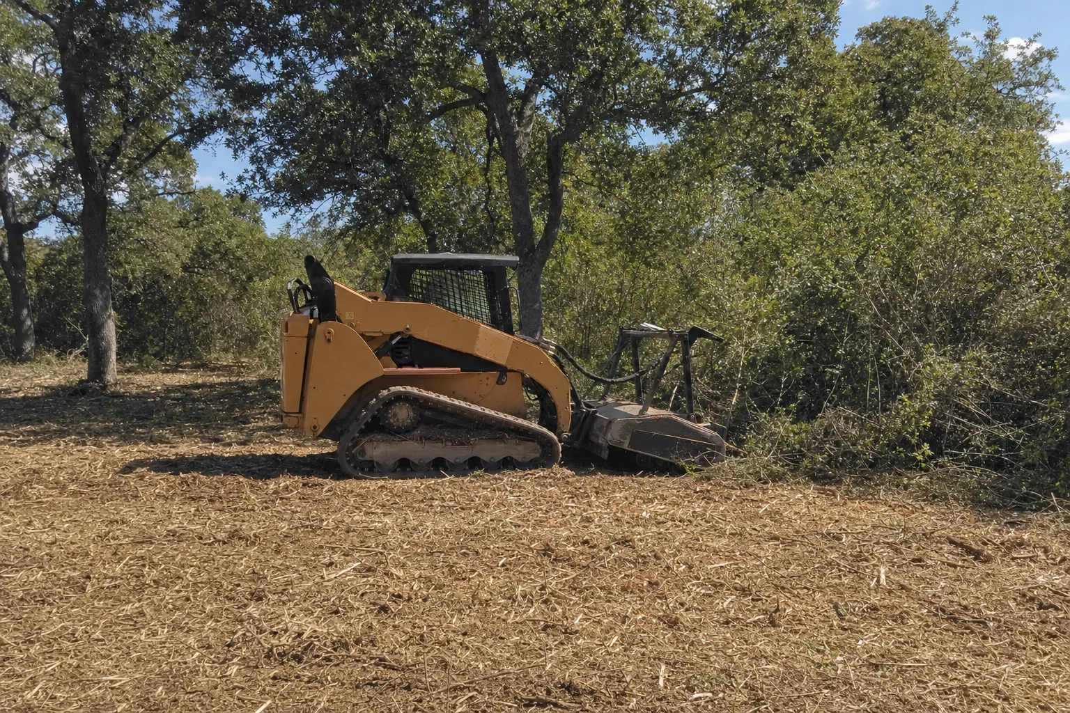 The tracked loader rests beside standing brush and a carpet of chips.
