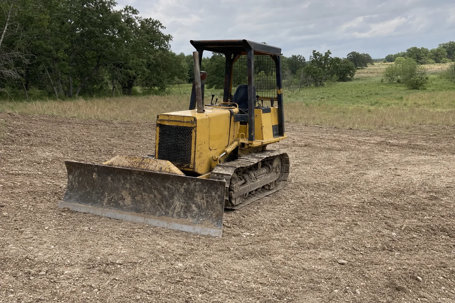 The dozer blade rests on rough grade beside the grassy low side.