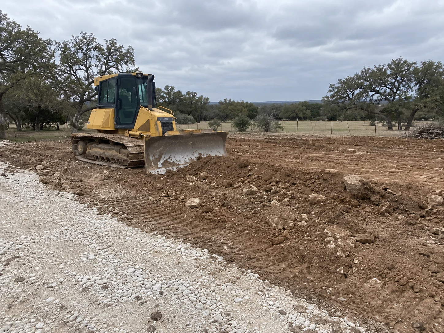 Yellow tracked bulldozer beside a rough homesite pad and gravel entrance.
